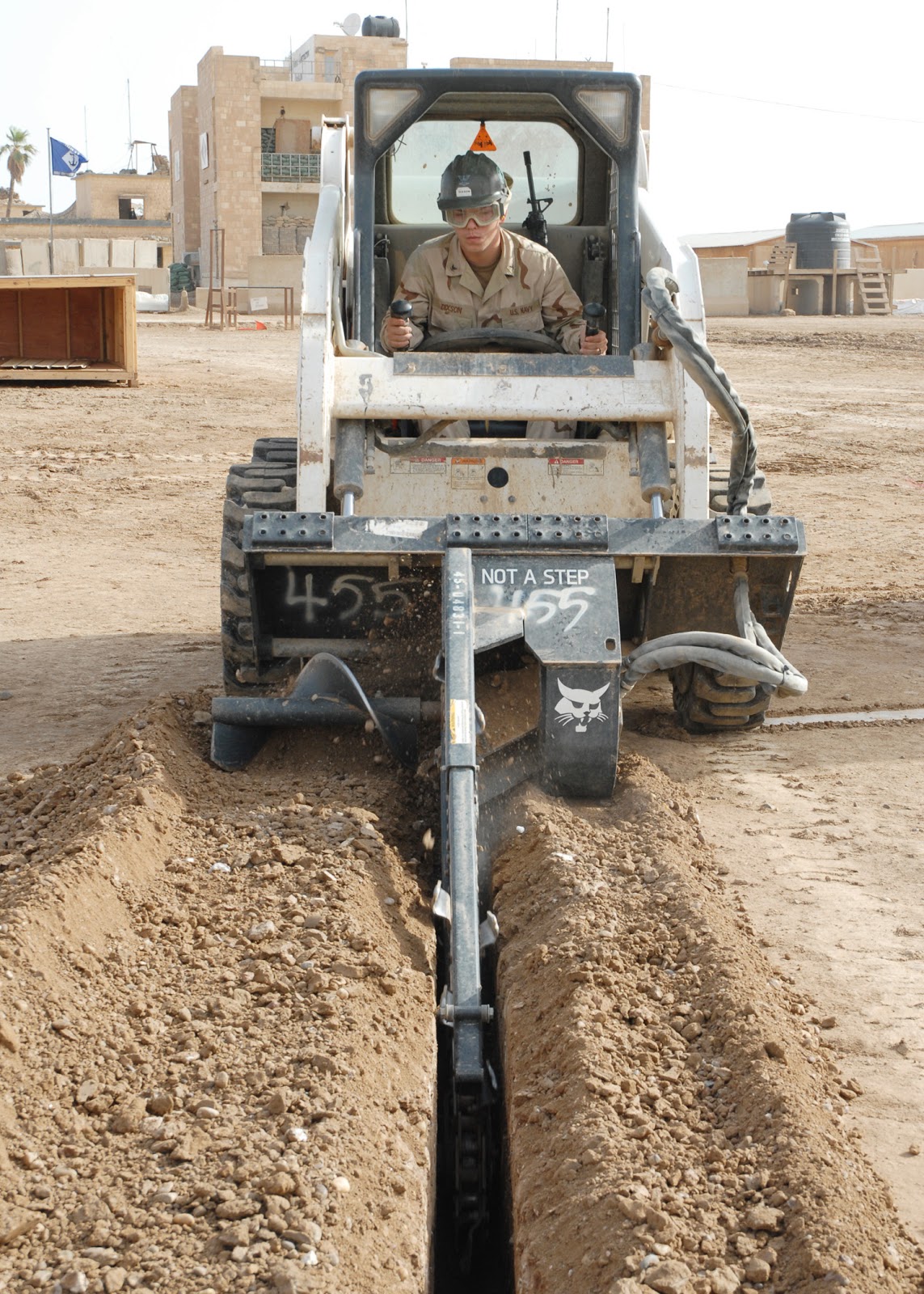 A person is operating a loader with hydraulic chain trenchers attachment