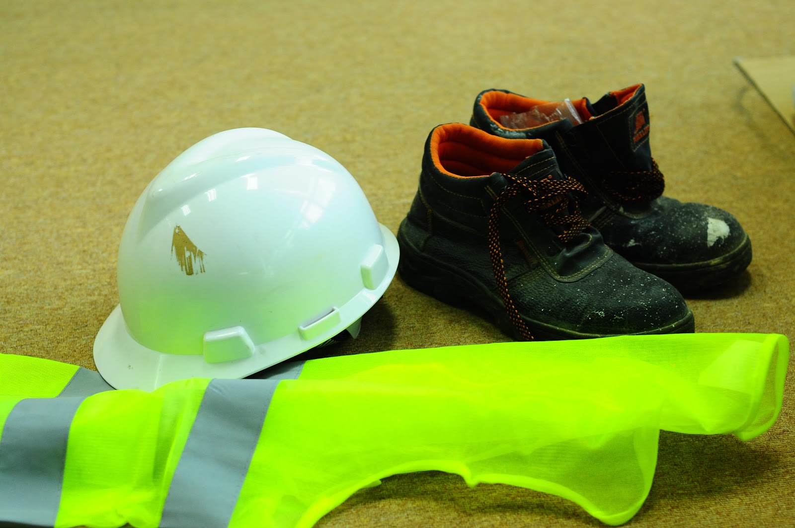 A safety hat, safety vest and safety shoes laid on the ground
