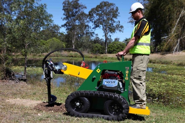 A man is operating micro loader with drill bit attachment