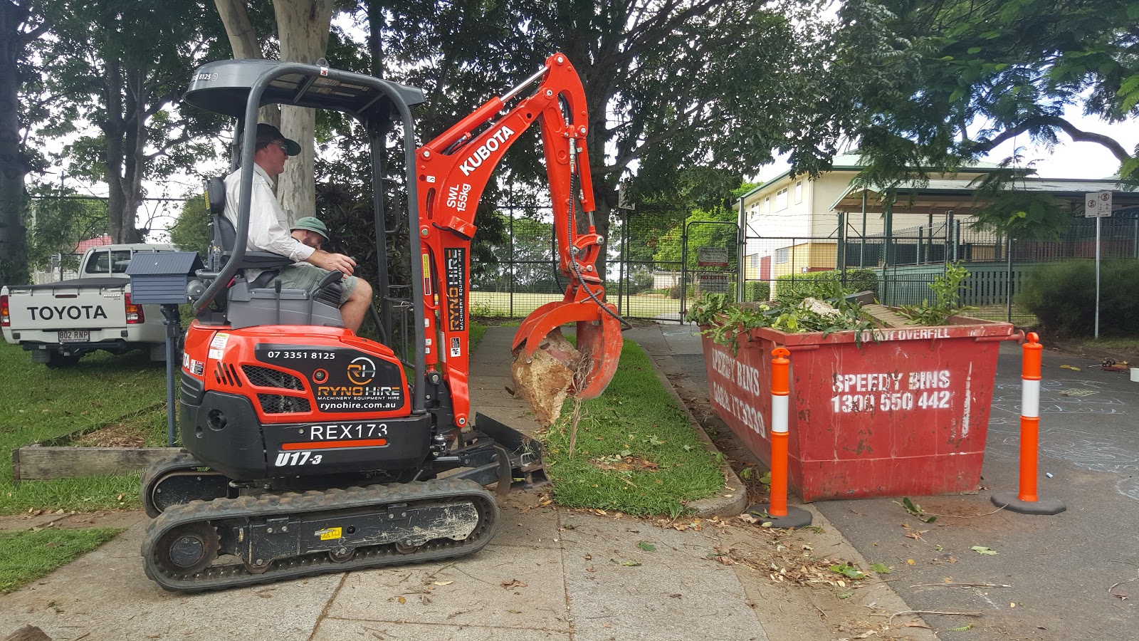 A man is operating an excavator with hydraulic rock grab to the bin area