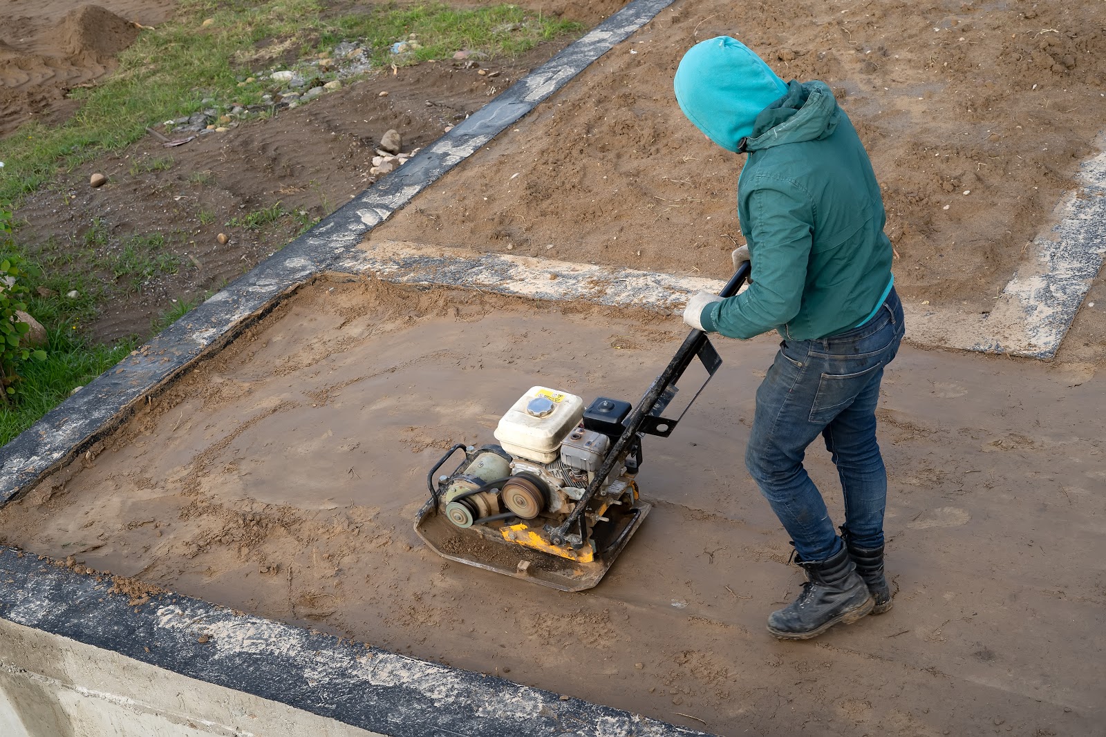 A person is operating vibrating plate on the soil