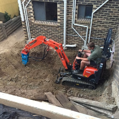 A man is operating a mini excavator at the house backyard