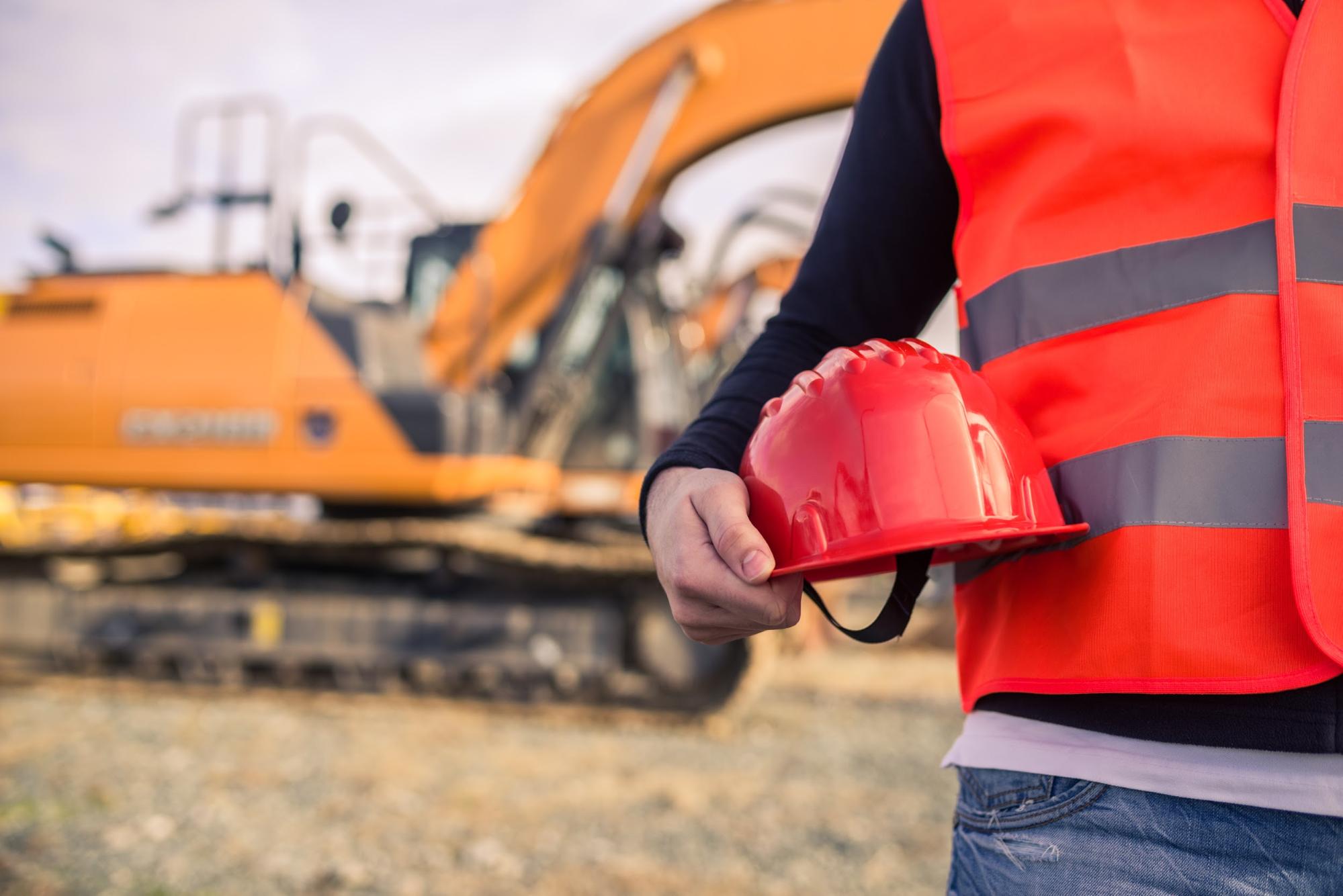A trader holds a red safety hat with excavator on the background