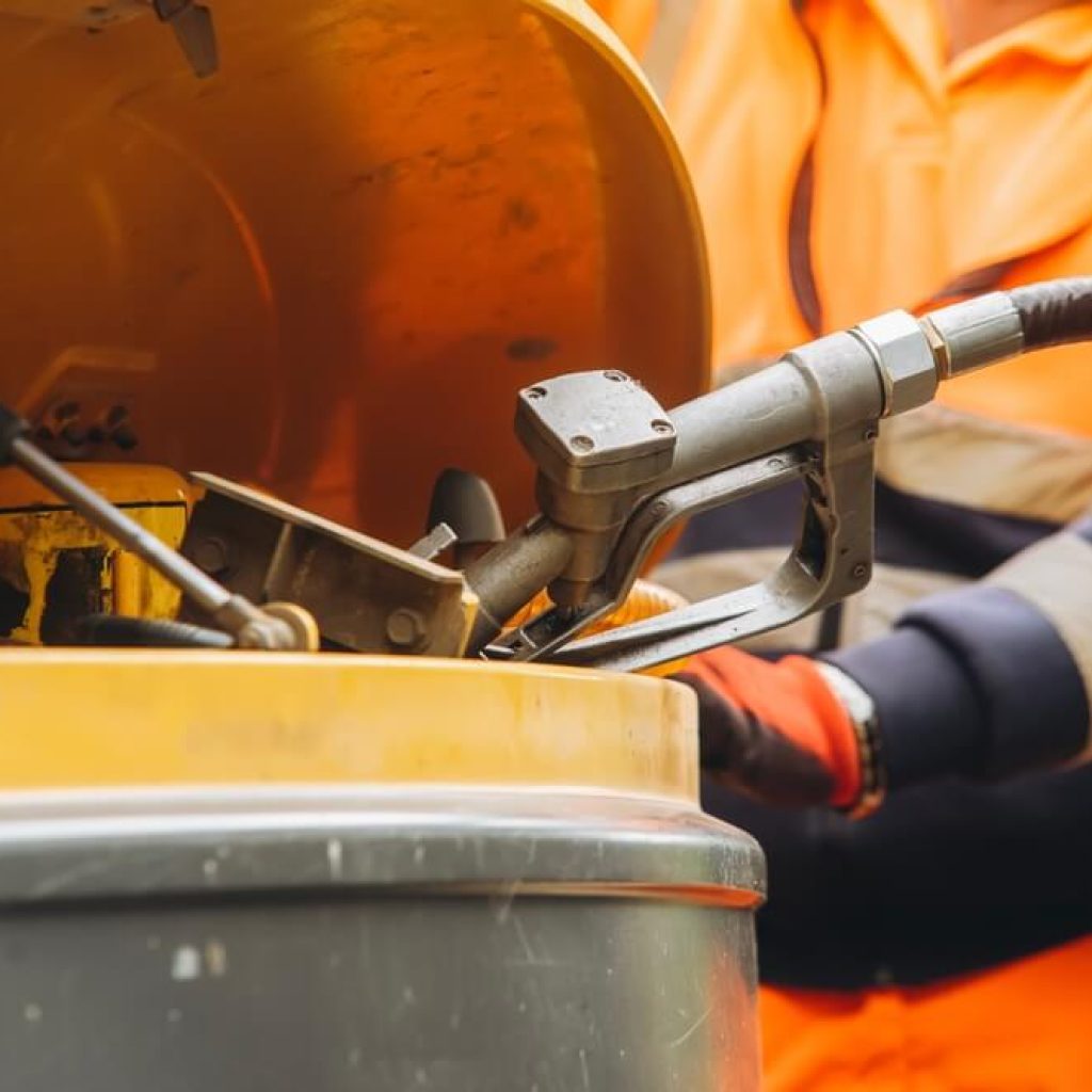 A person wearing high-vis holding a fuel pump to refuel a piece of yellow heavy machinery.