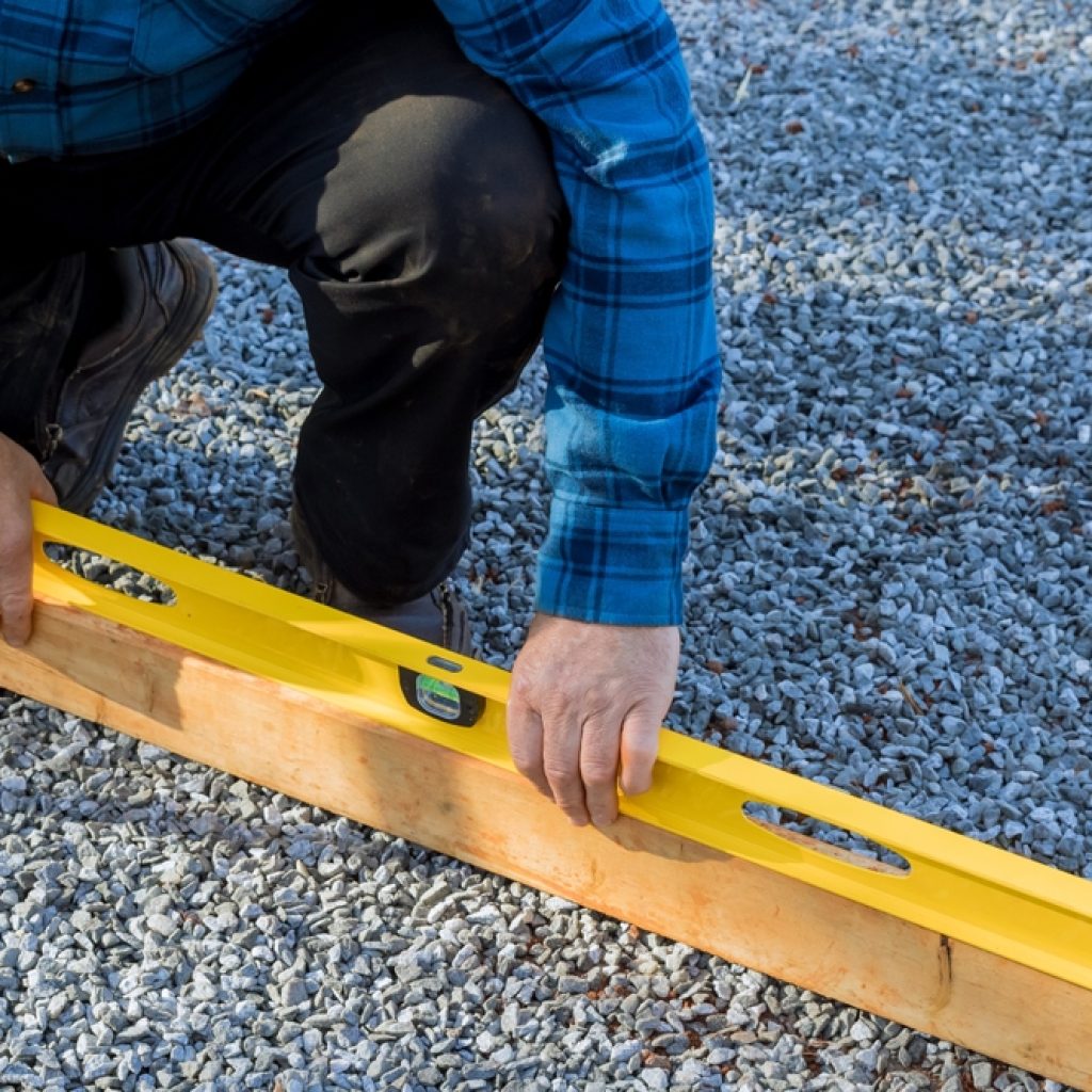 A man checking the gravel is level with a levelling tool for the foundation of a shed. 