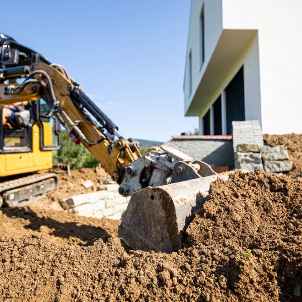 An excavator digging in the backyard of a house during a DIY project. 