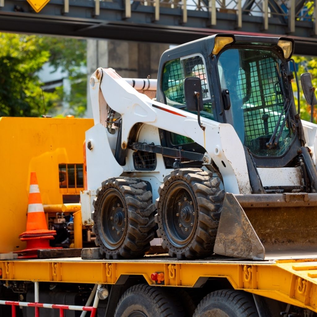A skid-steer loader on the back of a truck ready to be offloaded and used on a worksite.
