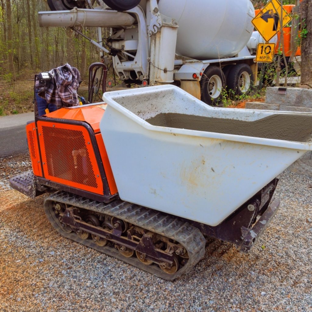 A mini dumper carrying cement with a cement truck in the background showing how to use a mini dumper.